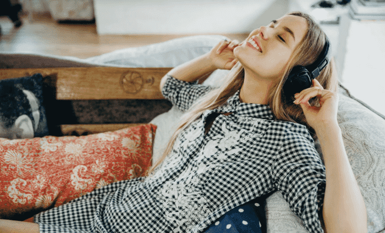 A girl lays on the couch and listens to music with her headphones.