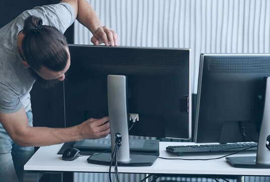 A man plugs a second monitor in at his home office.