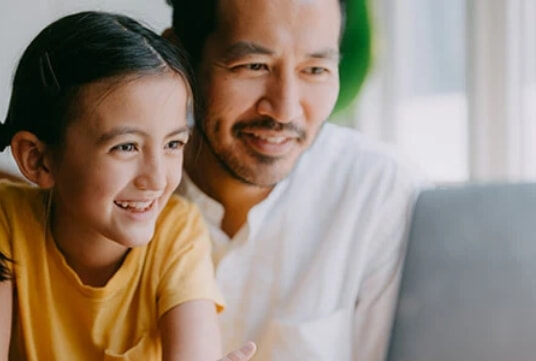 A father and daughter use a laptop together.
