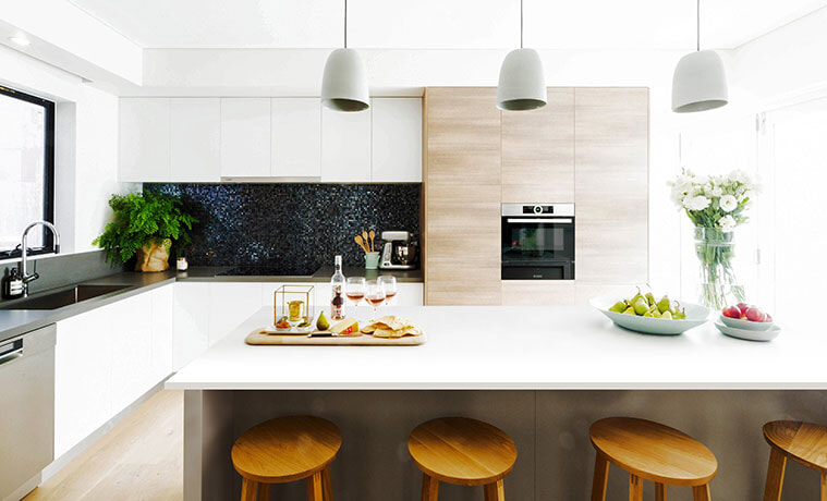 Modern open plan kitchen with chunky wooden stools and timber-look oven feature wall.