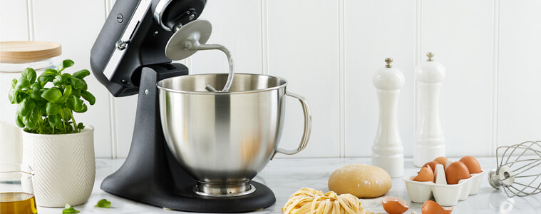 A matt black KitchenAid Artisan Stand Mixer sits in a white, modern kitchen on a grey benchtop.