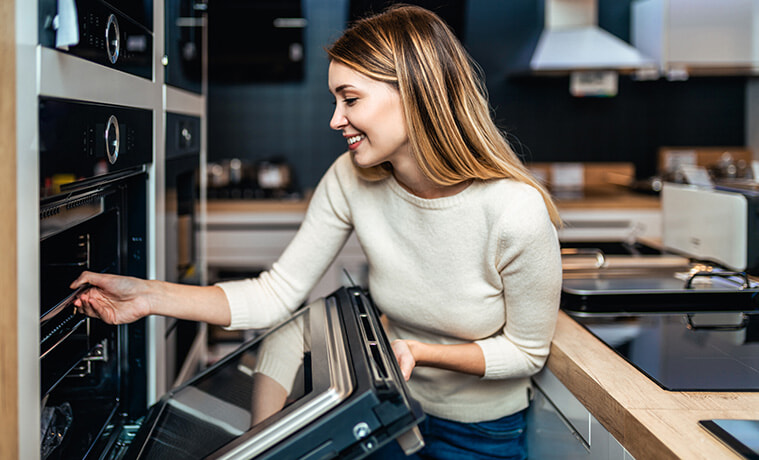 Woman opens the door of the wall oven in her modern kitchen.