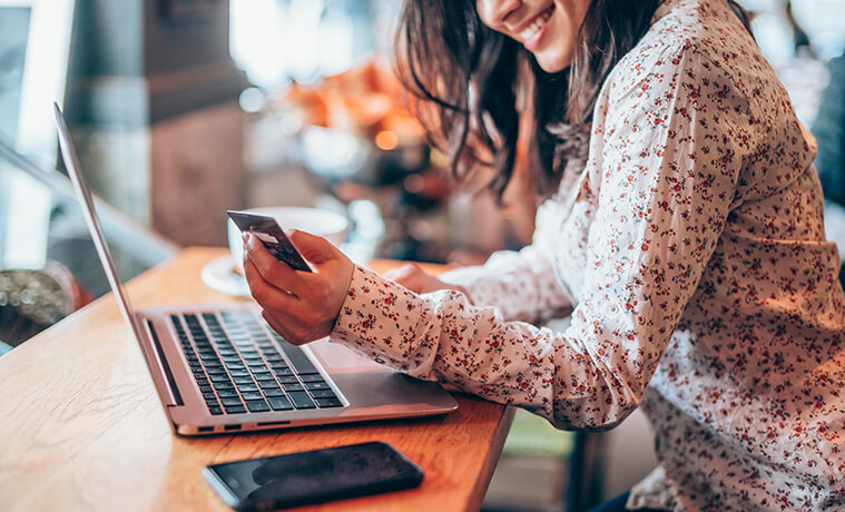 A woman in a cafe does some online shopping on her smartphone and laptop. 