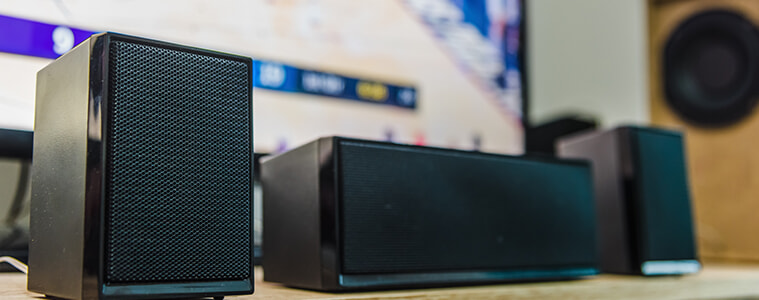 Home theatre speakers lined up at the base of a big screen TV. 
