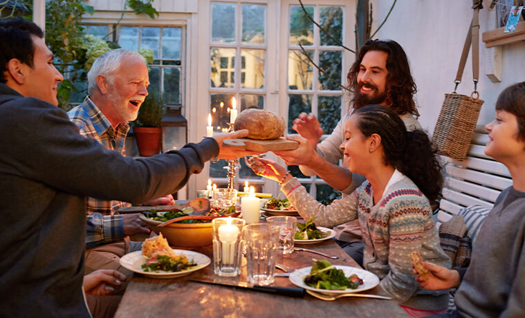 A big family having dinner together around a cosy table and passing a basket of bread to each other.